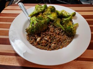 A plate of green lentils and green, charred broccoli sitting on a multicolored wood cutting board. 