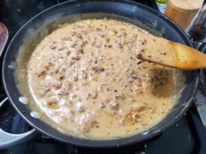 Sausage gravy in a non-stick skillet with a wooden spoon propped against it. 